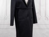a black coat on a mannequin stand in front of a white wall