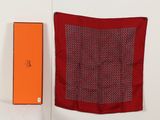 une boîte orange se trouve à côté d'une écharpe rouge sur une surface blanche