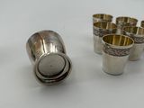 four silver shot glasses and a silver shot glass on a white surface