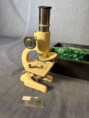 Un vieux microscope est posé sur une table, à côté d'une boîte.