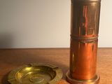 une petite tasse en laiton et un cendrier en laiton posés sur une table en bois