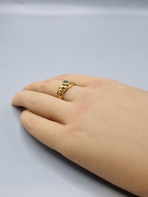 someone is holding a gold ring with a green stone on it