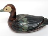 a small wooden duck that is sitting on a white surface