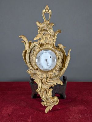 une horloge dorée posée sur un support rouge