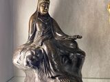 une statue représentant une femme assise sur un rocher à côté d'une horloge