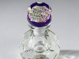 une petite bouteille en verre avec un bouchon violet et des paillettes dessus