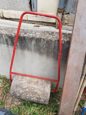 a red hand truck leaning against a wall next to a pile of wood