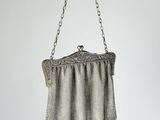 an antique silver mesh purse hanging from a chain on a white wall