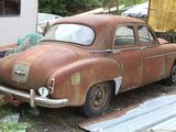 rusted old car sitting in a junkyard next to a trailer