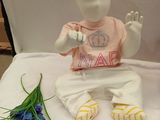a small doll sitting on a bed next to a blue flower