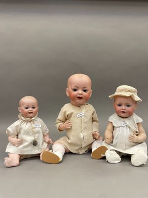 trois poupées représentant des bébés, assises les unes à côté des autres sur une table