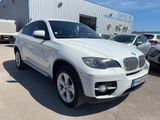 Le SUV BMW blanc est garé devant un immeuble.