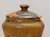 un petit pot marron muni d'un couvercle, posé sur une table