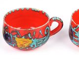 a red cup with a lid next to two mugs