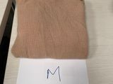 Le pull est de couleur beige et porte une étiquette sur laquelle est inscrit « m ».