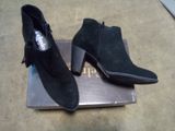 une paire de bottines noires en daim ornées de pompons, posées sur une boîte