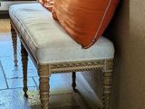 a bench with two orange pillows on it in front of a window