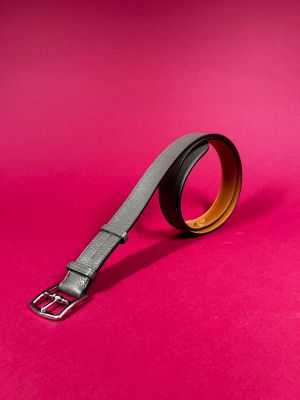 a black and brown belt with a metal buckle on a pink background