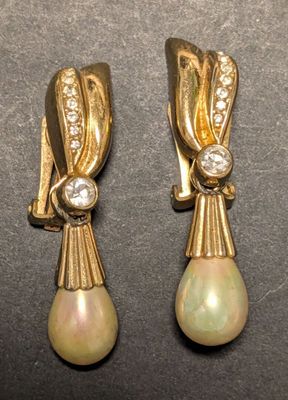 deux paires de boucles d'oreilles en perles et diamants posées sur un fond noir