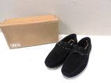 mocassins en daim noir pour homme, avec des boucles, posés sur une table