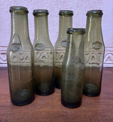 six bouteilles en verre vert vides posées sur une table en bois près d'un mur blanc