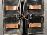 two pieces of black leather with brown leather straps on a gray surface