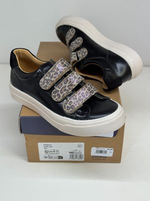 des baskets noires et blanches ornées de lanières à imprimé léopard, posées sur une boîte en carton