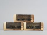 trois boîtes contenant des véhicules militaires miniatures, posées sur une surface blanche