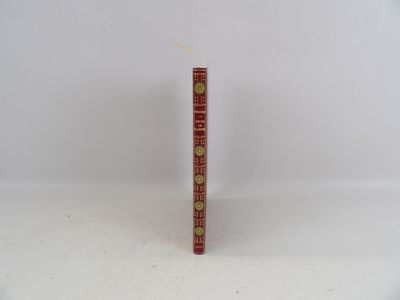 un livre rouge aux bords dorés posé sur une surface blanche