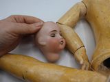 une main tenant une tête de poupée au-dessus d'un mannequin en bois