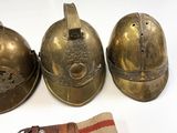 three antique brass helmets and a belt are sitting on a white surface