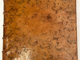 un vieux livre à la couverture marron posé sur une table blanche