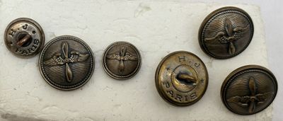 six boutons anciens en laiton posés sur un morceau de papier blanc