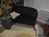 a black couch sitting in a living room next to a potted plant