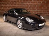 a picture of a black sports car parked in front of a brick wall