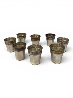 six silver shot glasses sitting on top of each other on a white surface