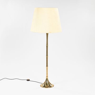 a gold floor lamp with a white shade on a white background