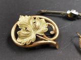 a gold brooch with a leaf on it next to two other brooches