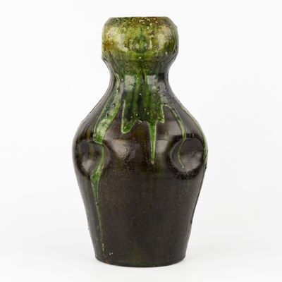un vase vert et noir posé sur une surface blanche
