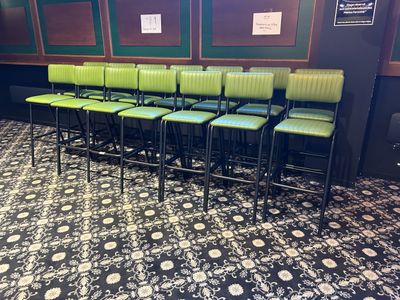 Des rangées de tabourets de bar verts sont disposées devant un mur orné de photos