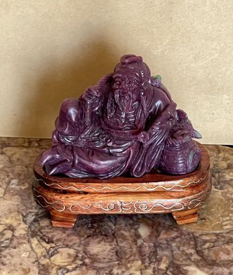 une statue violette posée sur un socle en bois, elle-même posé sur une surface en marbre