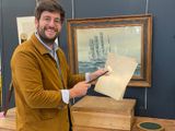 un homme souriant tenant un bout de papier devant l'image d'un bateau
