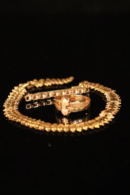 a close up of a gold necklace and a ring on a black surface