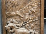 plaque en bois sculptée représentant un homme à cheval tirant une charrette sur laquelle se trouve un autre homme