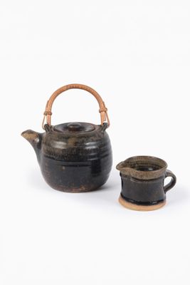 une petite théière et une tasse posées sur une surface blanche