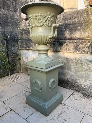 un grand vase vert posé sur un socle sur le trottoir