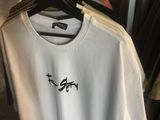 un t-shirt blanc orné d'un oiseau noir, suspendu à un portant dans un magasin de vêtements