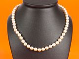 a white pearl necklace on a black mannequin with orange background