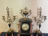 une horloge posée sur une table, à côté de trois chandeliers