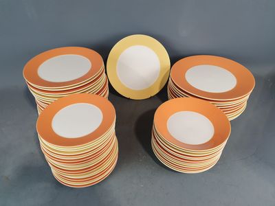 douze assiettes plates orange et blanches à bord doré posées sur une table